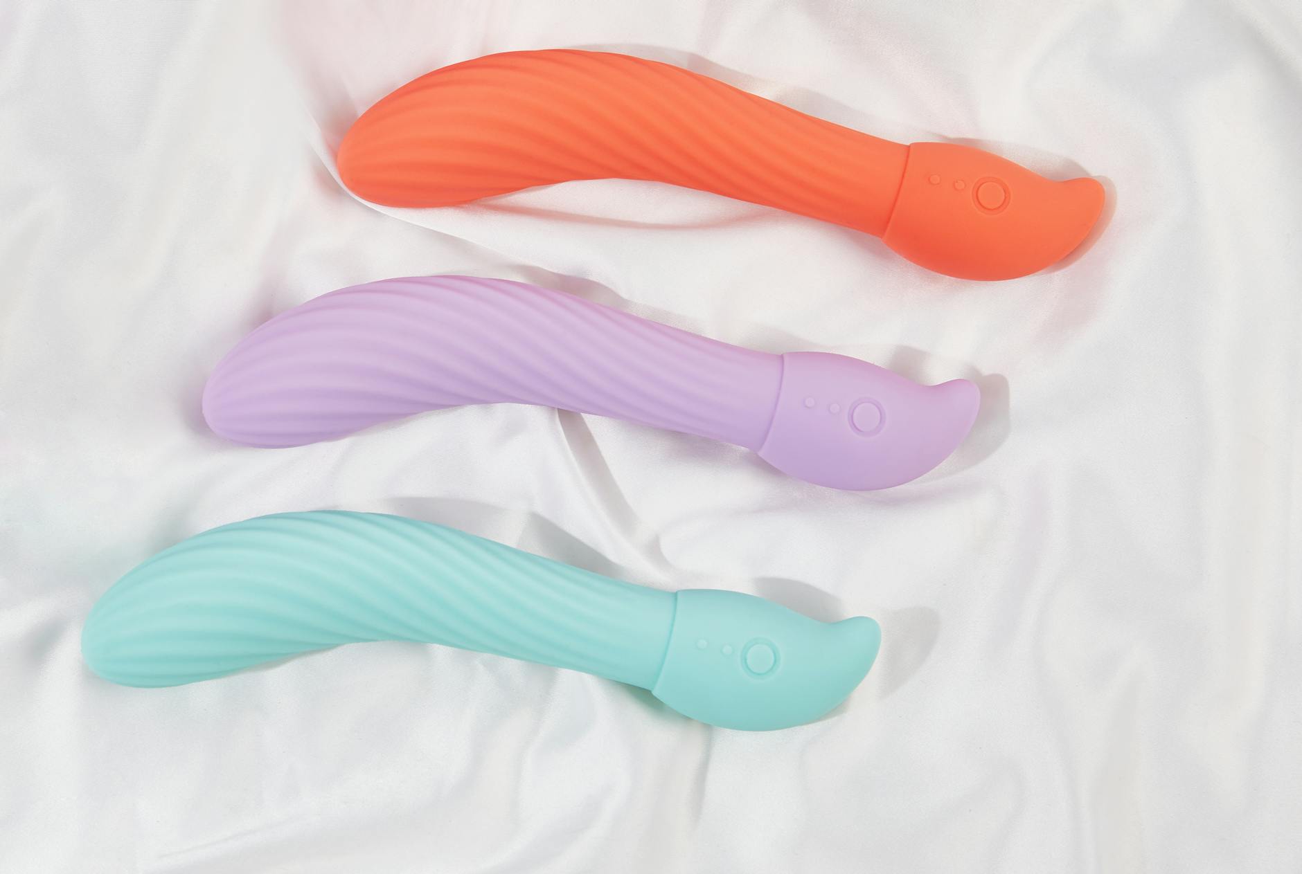 Three colorful clitoral vibrators arranged on white fabric, highlighting their smooth texture and design.