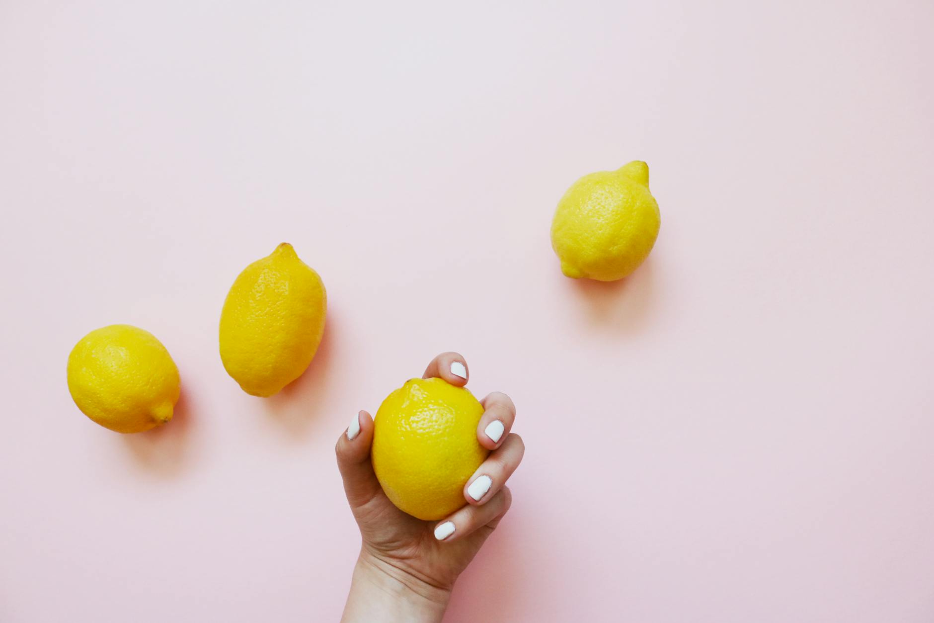 A hand holding a fresh lemon on a soft pink background, symbolizing renewal and natural pleasure.