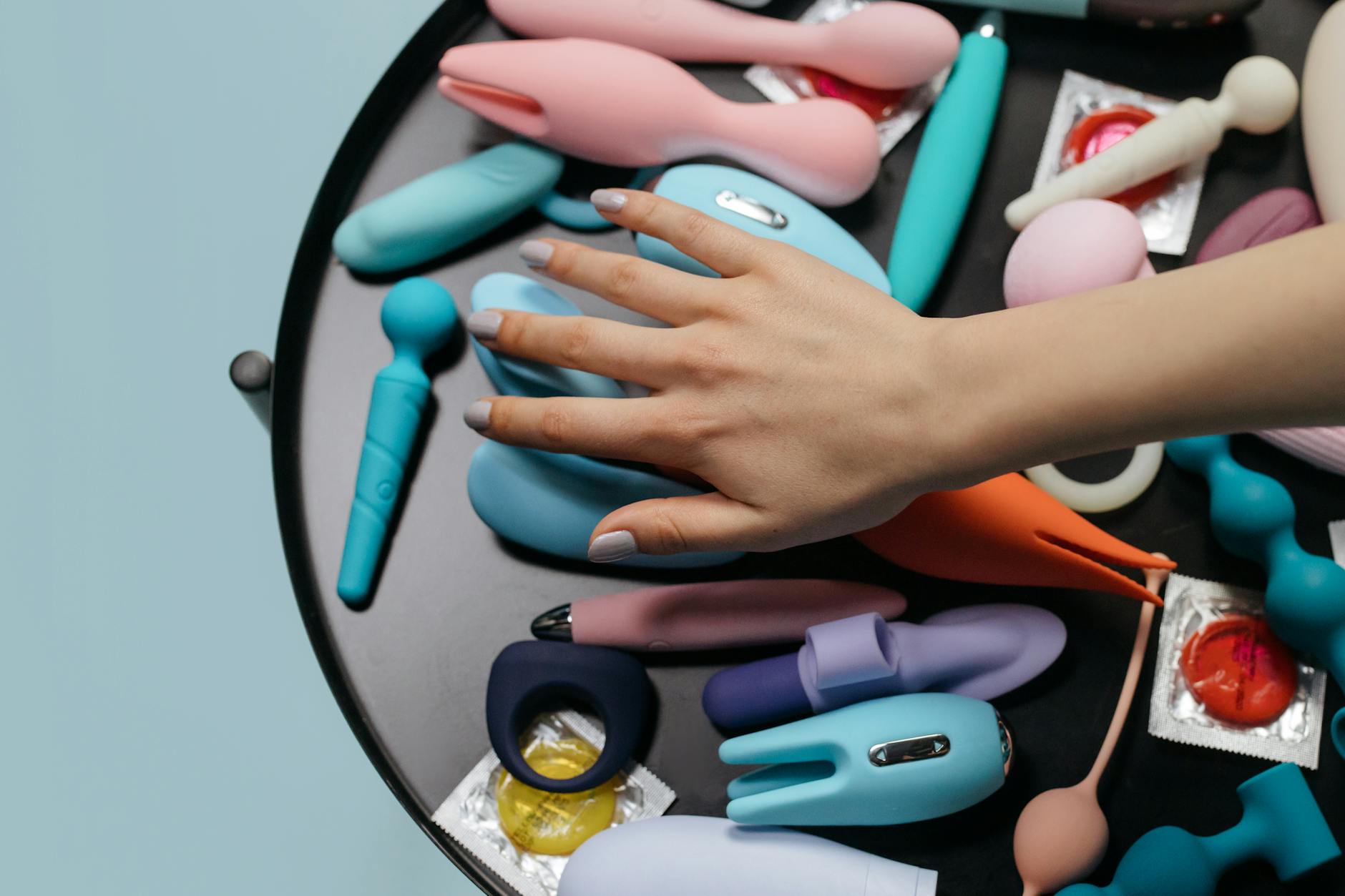 Hand reaching over a collection of colorful silicone vibrators on a table