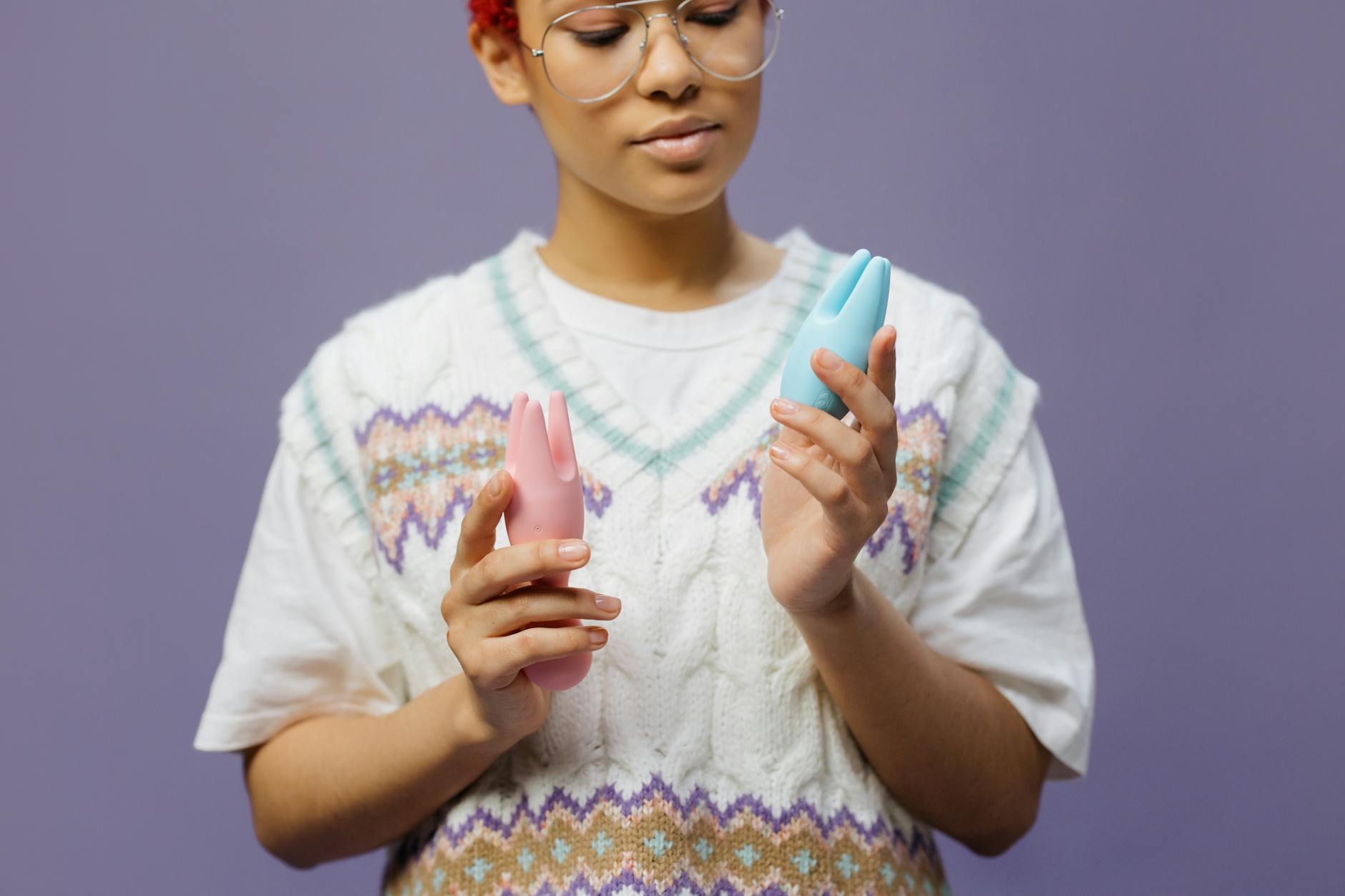 Woman holding blue and pink silicone vibrators thoughtfully, exploring pleasure during perimenopause.