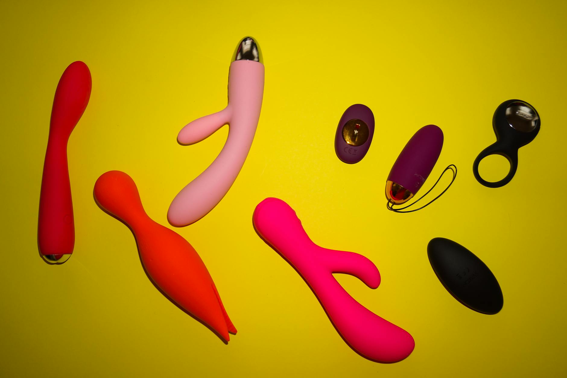 Colorful adult toys arranged on bright yellow surface, including the Lem clitoral vibrator
