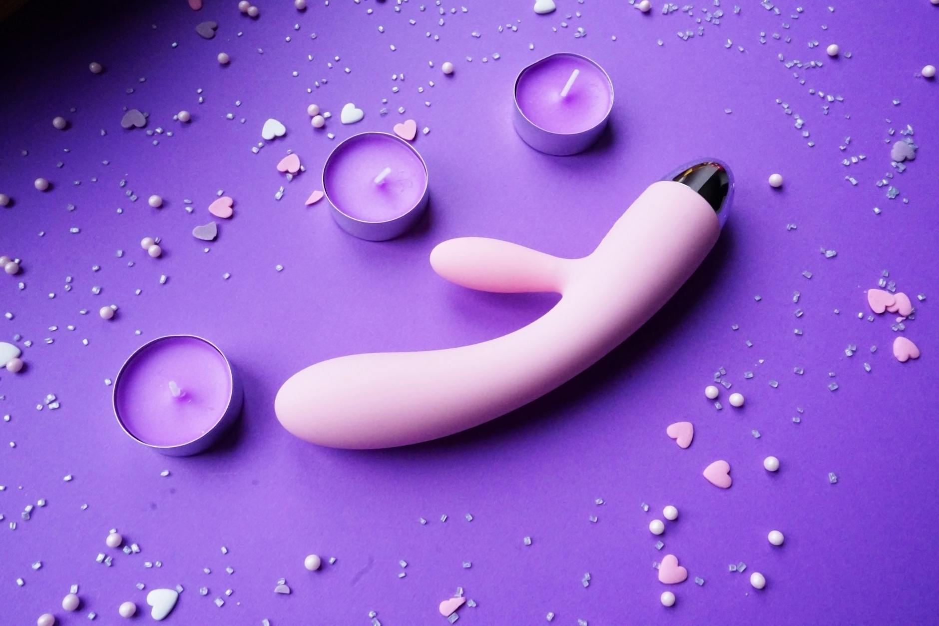 Pink vibrator on purple background with heart confetti and candles for romantic intimate setting